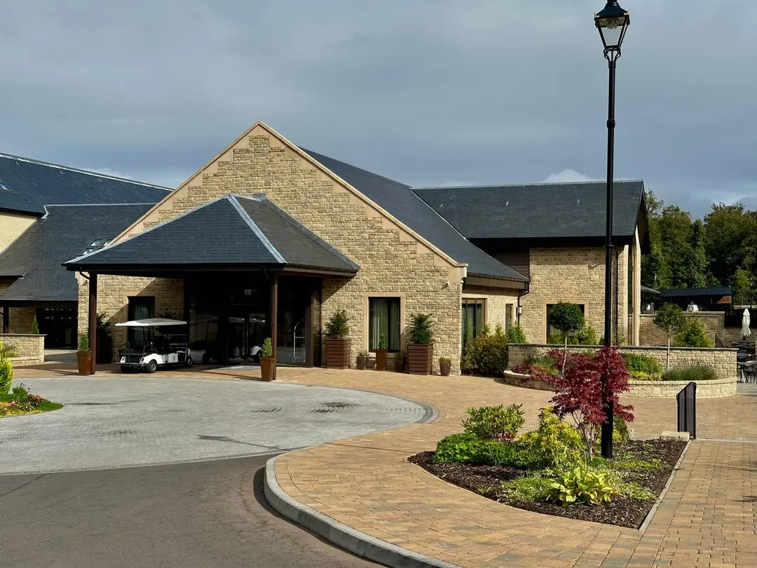 The new hotel building at Crossbasket: modern sandstone under slate roofs, with a golf buggy parked beneath the covered entrance.