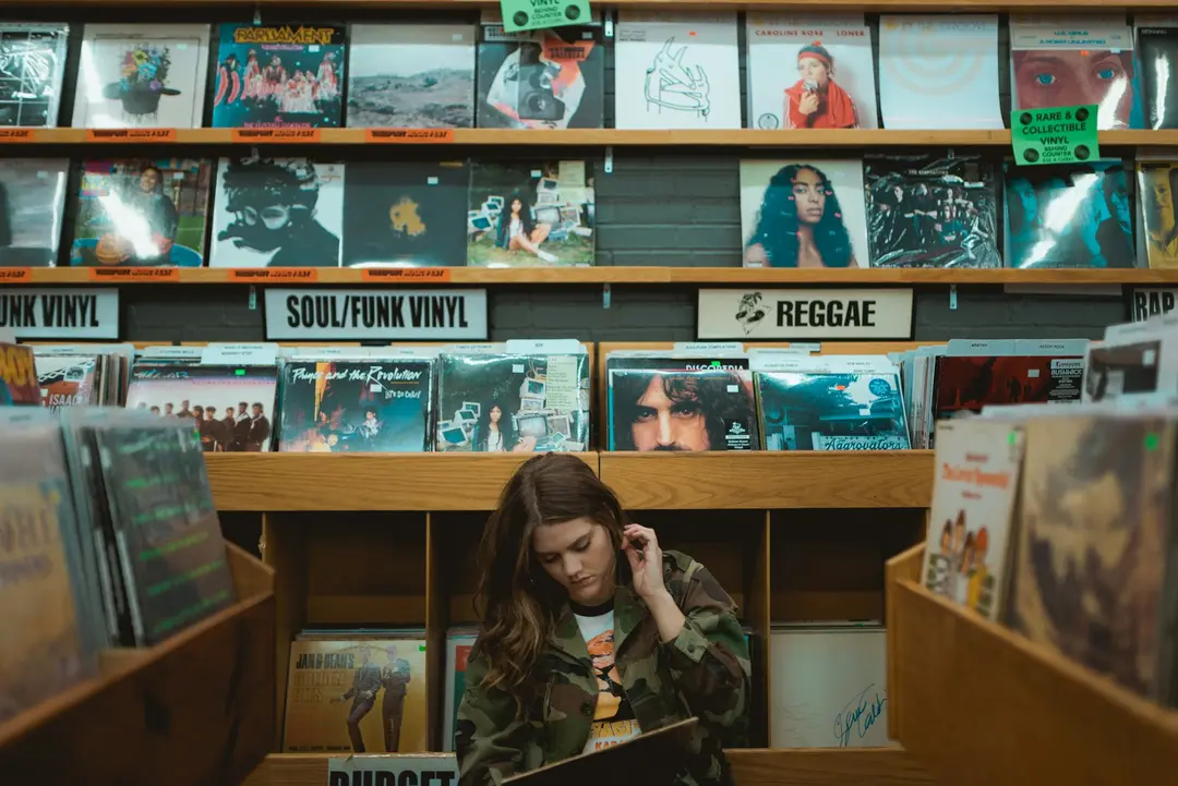 A woman browsing albums in a record shop, in front of shelves of vinyl sorted into sections such as Soul/Funk and Reggae